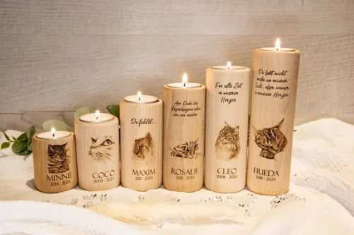 Trauerlicht Katze rund, aus Holz, Höhen 6 cm -16 cm, mit brennenden Teelichtern. Graviert mit verschiedenen Katzenmotiven, Namen der Katzen, Geburts- und Sterbejahre. Dekoriert auf einem Holztisch mit Herzen und Zweigen.