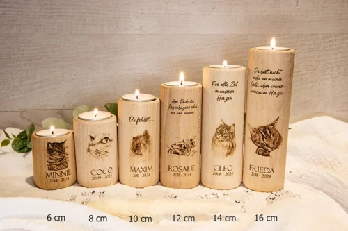 Trauerlicht Katze rund aus Holz, Höhen 6 cm -16 cm, mit brennenden Teelichtern. Graviert mit verschiedenen Katzenmotiven, Namen der Katzen, Geburts- und Sterbejahre. Dekoriert auf einem Holztisch mit Herzen und Zweigen. Mit Höhenangaben.