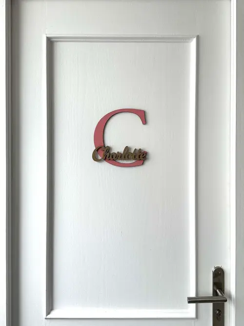 Einzigartige Namensschilder für die Zimmertüre aus MDF, zweifarbig lackiert. Das Türschild besteht aus einem 20 cm großen Buchstaben C und dem ausgeschriebenen Namen Charlotte, fixiert auf dem Großbuchstaben. Befestigt an einer weißen Türe.