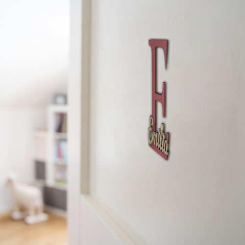 Einzigartige Namensschilder für die Zimmertüre aus MDF, zweifarbig lackiert. Das Türschild besteht aus einem 20 cm großen Buchstaben E und dem ausgeschriebenen Namen Emilia, fixiert auf dem Großbuchstaben. Befestigt an einer weißen Türe.